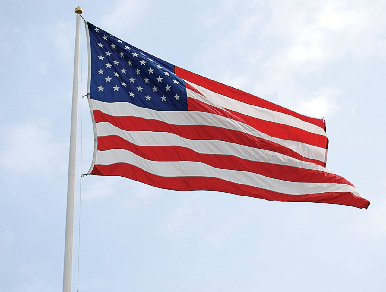 5' x 9.5' American Flag - Nylon US Flag with Embroidered Stars and Sewn Stripes flying on a pole against a clear sky.