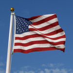 Close-up of an American Flag flying, featuring embroidered stars and sewn stripes, with brass grommets for durability, suitable for indoor or outdoor use.