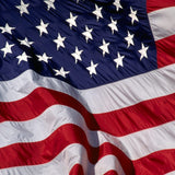 Close-up of an American Flag with embroidered white stars and sewn stripes, featuring strong canvas header and brass grommets for durability.