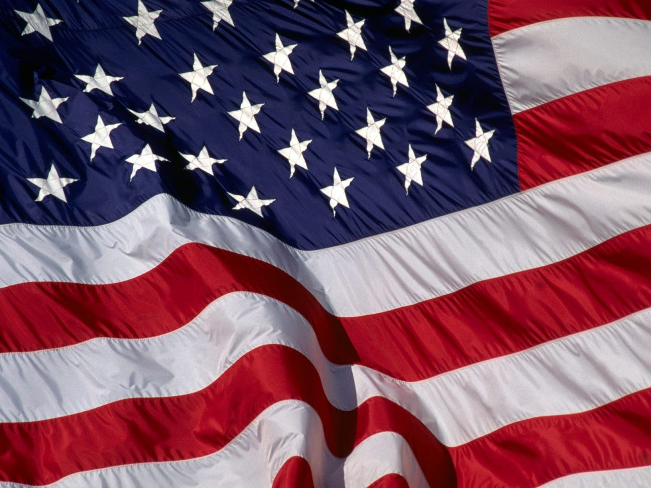 Close-up of an American Flag with embroidered white stars and sewn stripes, featuring strong canvas header and brass grommets for durability.