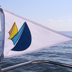 Custom SEWN Applique PENNANT displayed on a boat, featuring a detailed logo, reinforced header and brass grommets, showcasing quality craftsmanship and durability.