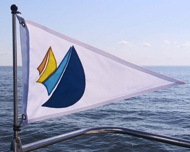 Custom SEWN Applique PENNANT displayed on a boat, featuring a detailed logo, reinforced header and brass grommets, showcasing quality craftsmanship and durability.